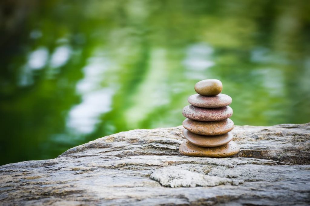 Pile de pierres zen équilibrées sur une roche, avec un arrière-plan flou d'eau verte, symbolisant la tranquillité et l'harmonie dans la nature.